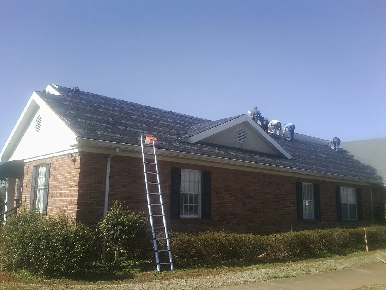 Crew tearing shingles off a brick ranch roof with a ladder set — Emergency Roof Repair work by our crew in Mertztown