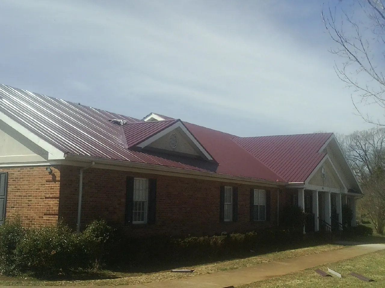 Red metal roof with gabled entries on a long brick building, from a Hail Damage Roof Repair job in Mertztown