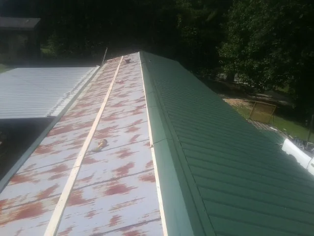 Old rusted panels beside newly installed green metal roofing — Wind Damage Roof Repair by Roofing Brothers in Mertztown