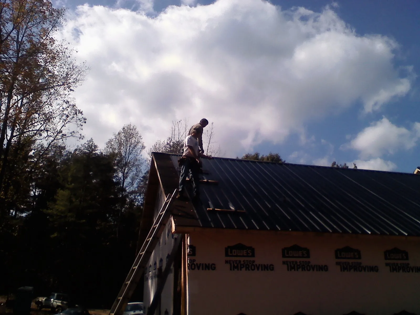 Roofer fastening dark metal panels high against a cloudy sky, from a Roof Inspection job in Mertztown