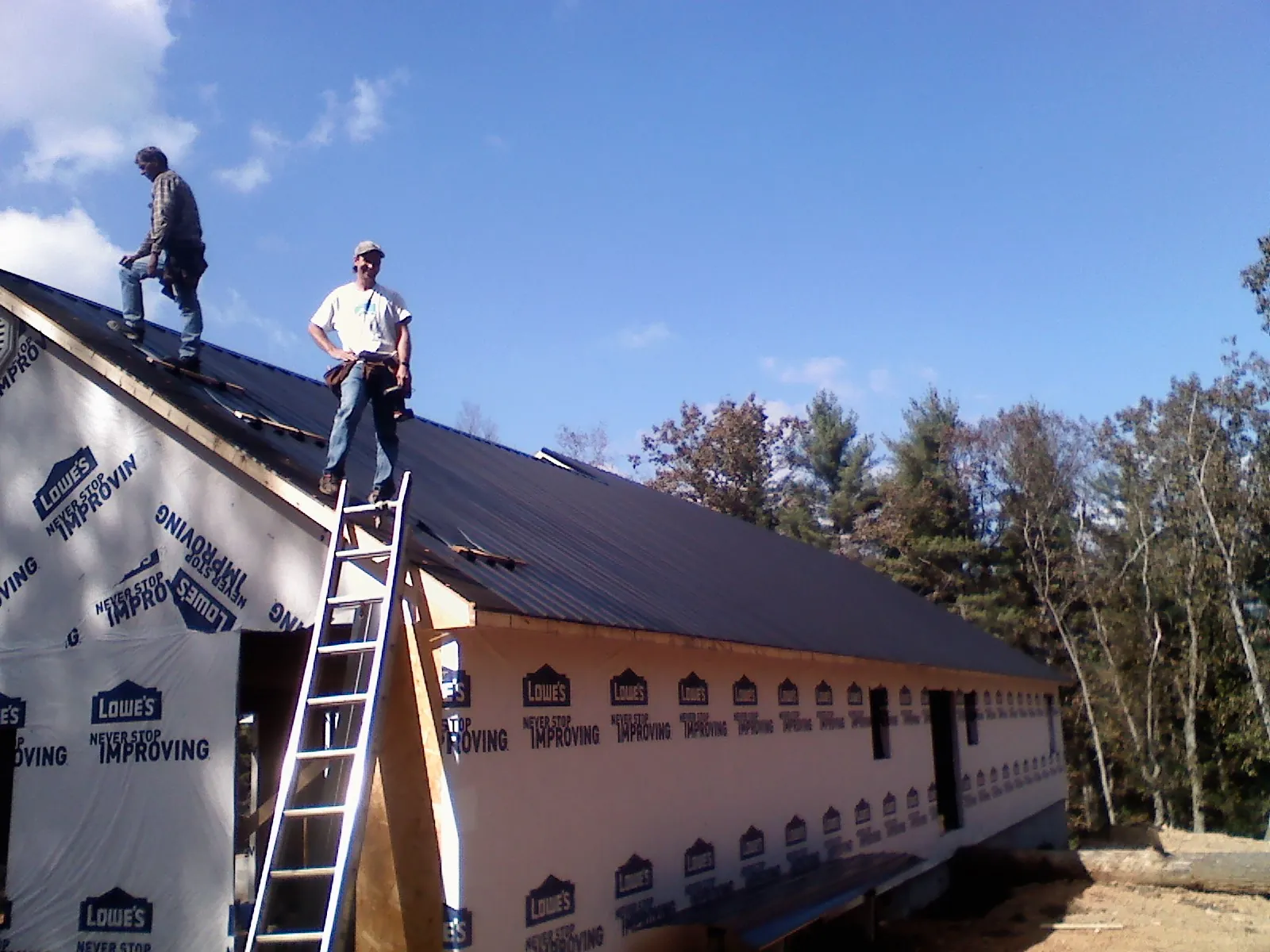 Two roofers standing on a long dark metal roof over a wrapped building in Mertztown