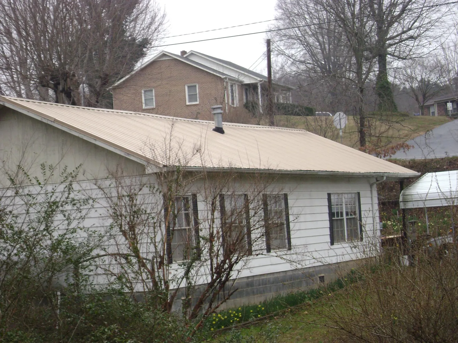 Tan metal roof on a white sided house set into a hillside — Commercial Roofing by Roofing Brothers in Mertztown